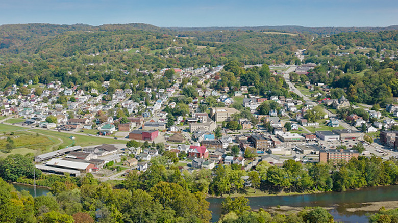 Aerial view of Apollo, Pennsylvania, with the tree-lined Kiski River in the foreground, several streets lined in homes and buildings, and tree-covered hills in the background, under a blue sky