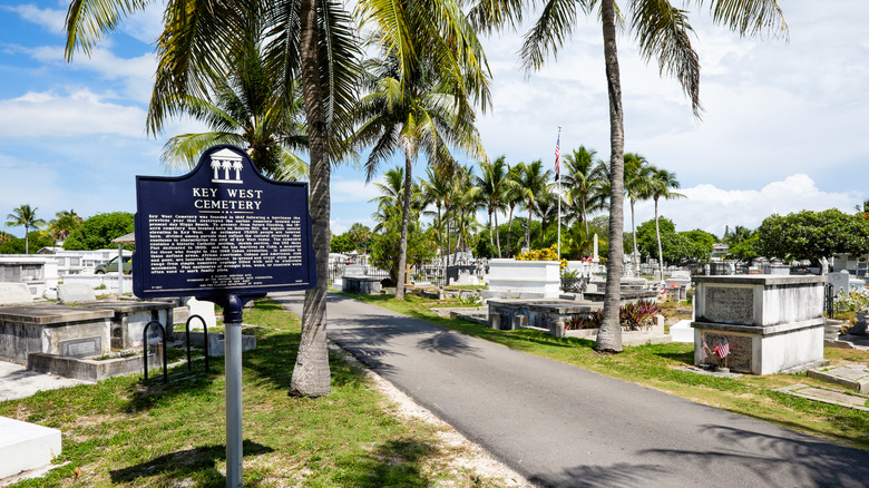 Sign in front of pathway with palm trees and tombs in Key West Cemetery