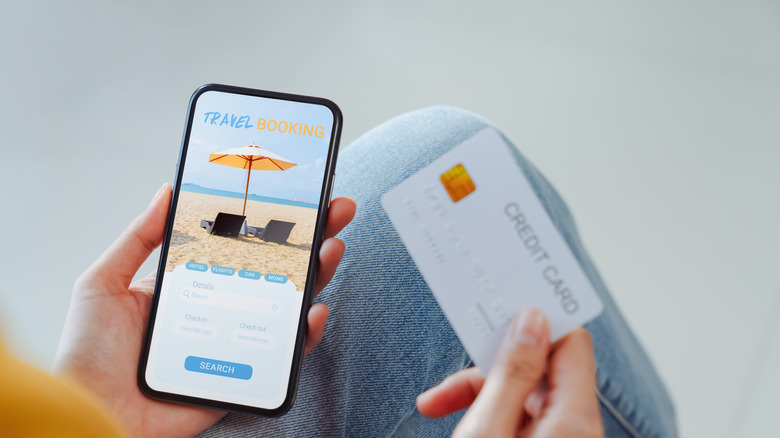 Hands holding a credit card and smartphone open to a travel booking page