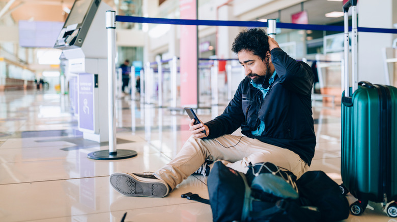 Man looking at his phone while sitting on the floor in an airport
