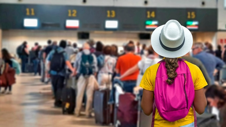 Traveler with pink backpack facing a long airport check-in line