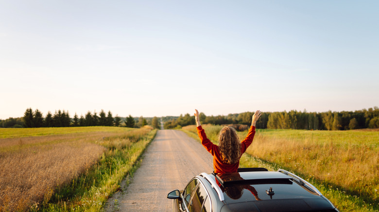 A woman leans out of her car on a roadtrip