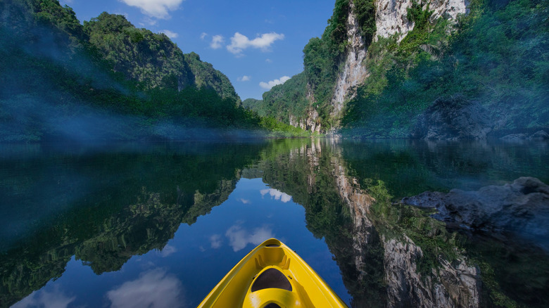 The tip of a yellow kayak on clear water mirroring the surrounding mountains