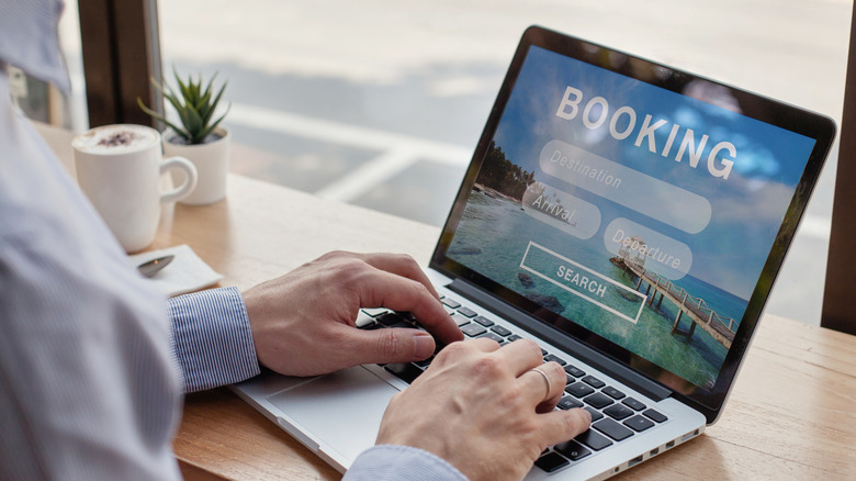 A man types on a laptop with a generic flight booking website open on the screen