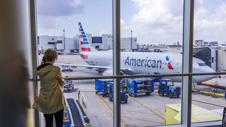 A woman talks on the phone while looking at an American Airlines plane outside the airport window