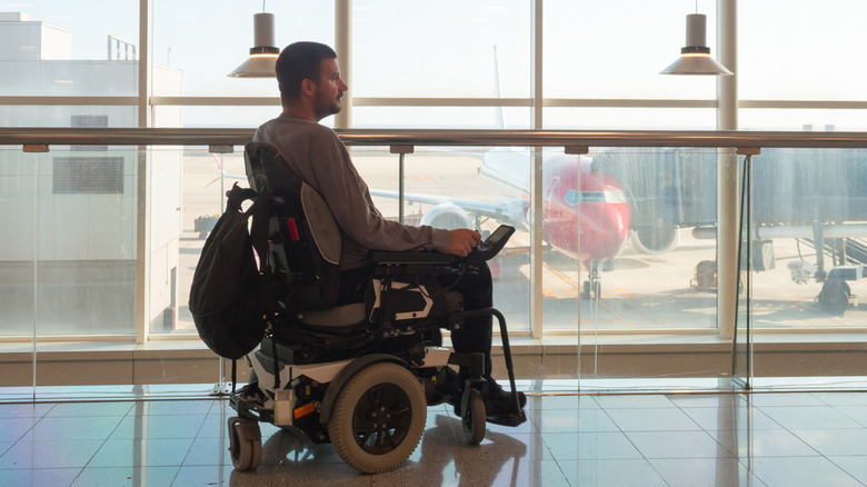 man in a wheelchair watches planes through an airport window