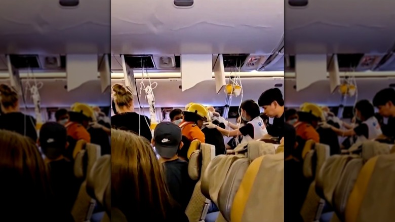 Scenes inside a plane following the aftermath of severe turbulence, showing damaged overhead panels, deployed oxygen masks, and ground medical personnel helping passengers