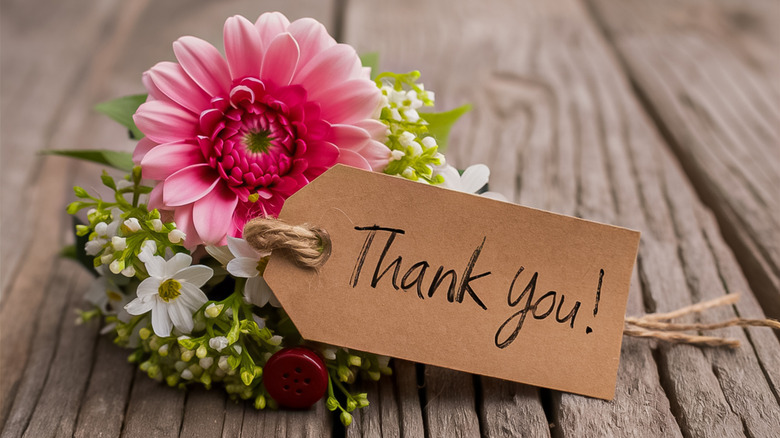 Thank you note attached to flower on a wooden background