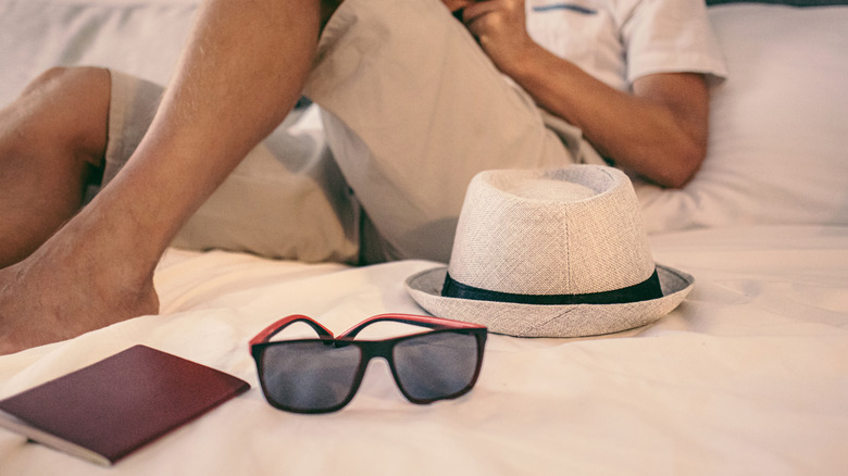 A man sitting next to his hat and passport on a hotel bed