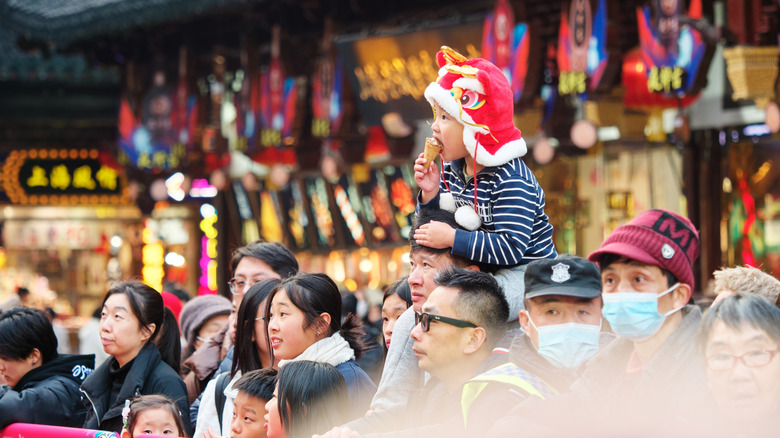 Child on his father's shoulders wearing a red dragon hat