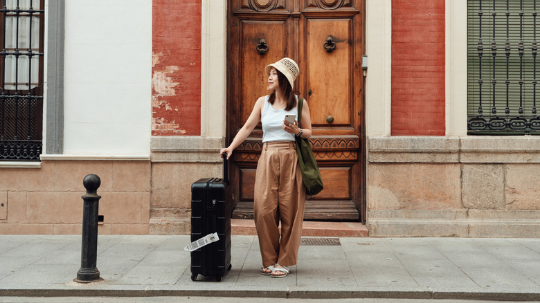 Woman standing on the side of the street with a suitcase
