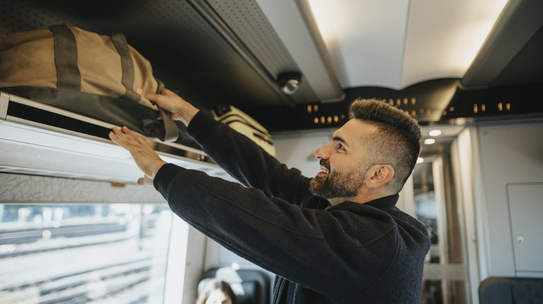 Traveler stowing his luggage in an overhead bin