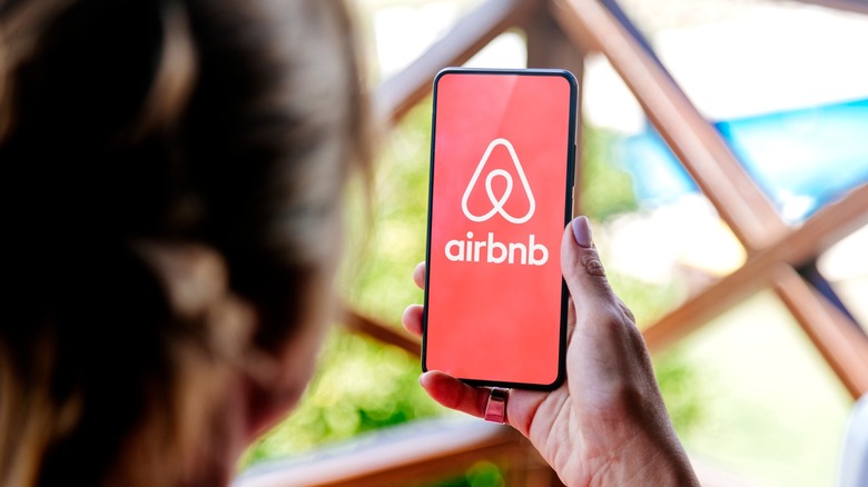 A woman holds a phone that shows the Airbnb logo