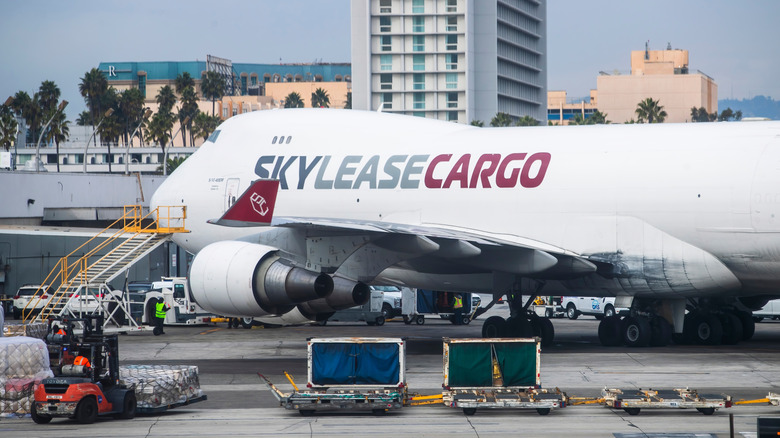 A Boeing cargo plane, parked on the tarmac and surrounded by cargo and equipment at an airport terminal
