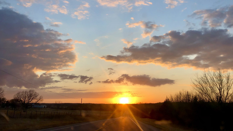 sunset with blue sky and clouds over rural field and open road