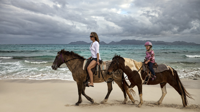 Mother and daughter riding horses on a beach