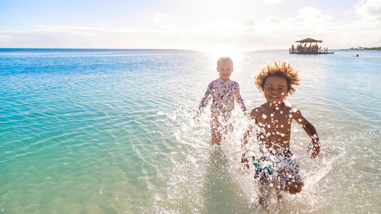 Little boy with curly hair and young girl splash in the Caribbean sea at sunset