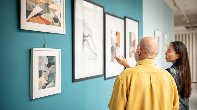 A curator showing a man geometric art in an uncluttered gallery.