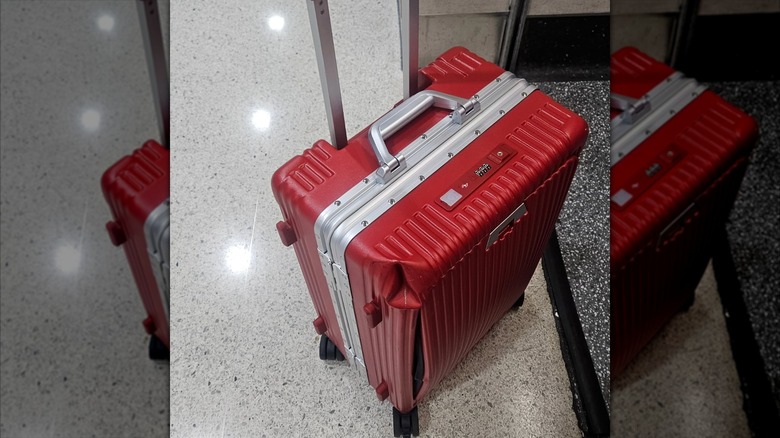 Red Nobl suitcase with a corner dented in and split down the side.