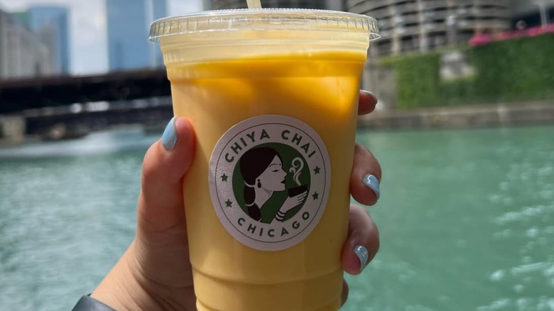 Someone holding an iced Chiya Chai beverage with the Chicago River in the background