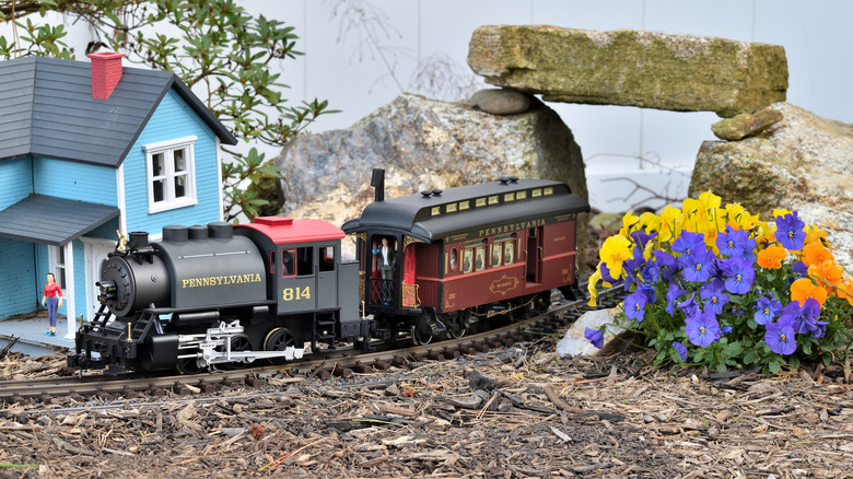 Miniature train moving under rock bridge and past model house