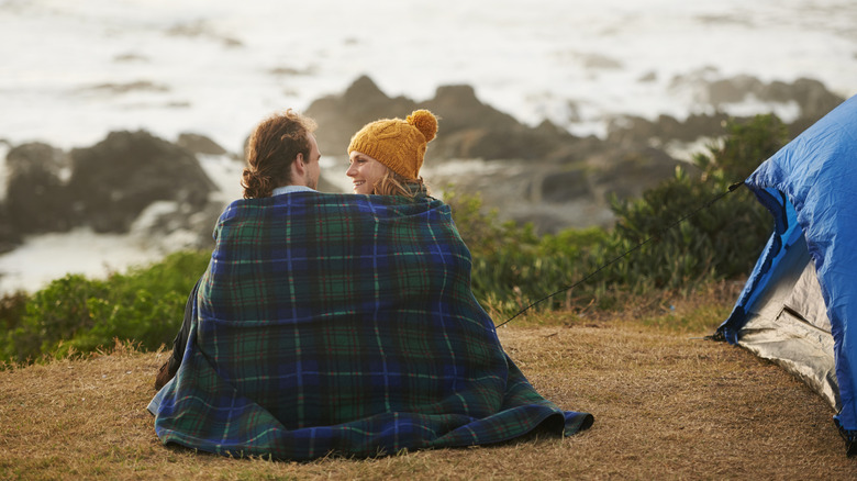 Couple sitting with a blanket around them on a bluff overlooking the ocean