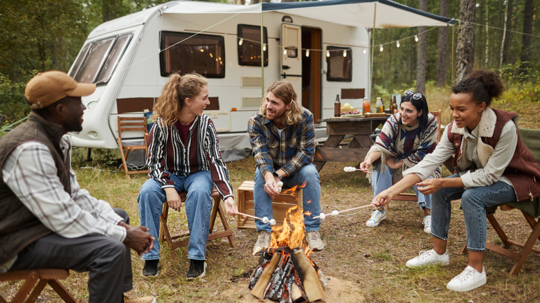 People making s'mores in front of an RV with lights strung up