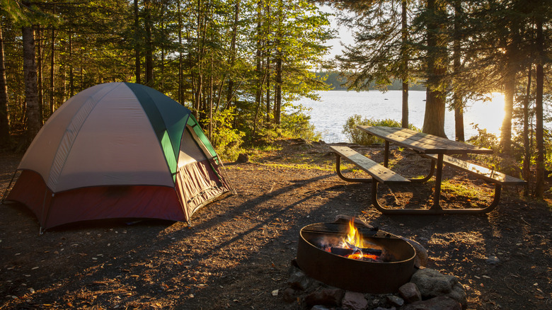 A tent set up by a lake with a campfire in the foreground