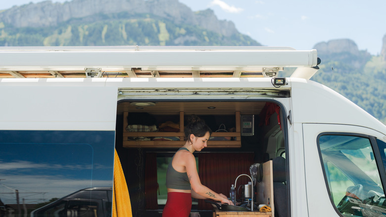 A woman cooking in a van with a mountain backdrop
