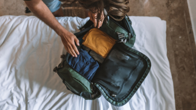 Person packing duffel bag on bed