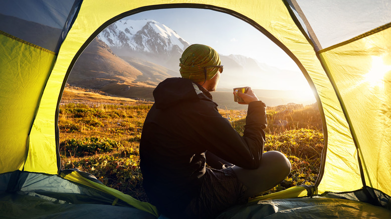 A man tent camping in the mountains and drinking hot tea