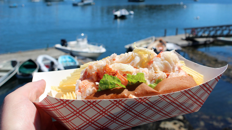 Hand holding lobster roll against a waterfront