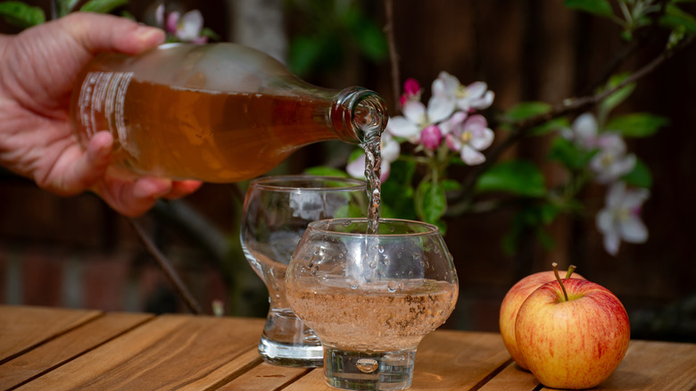 Server pouring a glass of Normandy cider into two glasses.