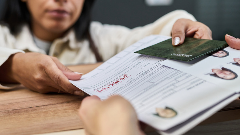A woman hands over a rejected visa form to an applicant