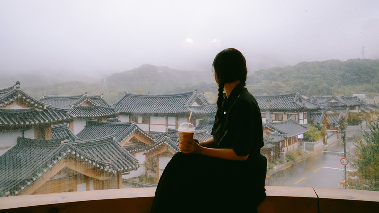Woman with a coffee looking out at a Korean neighborhood.