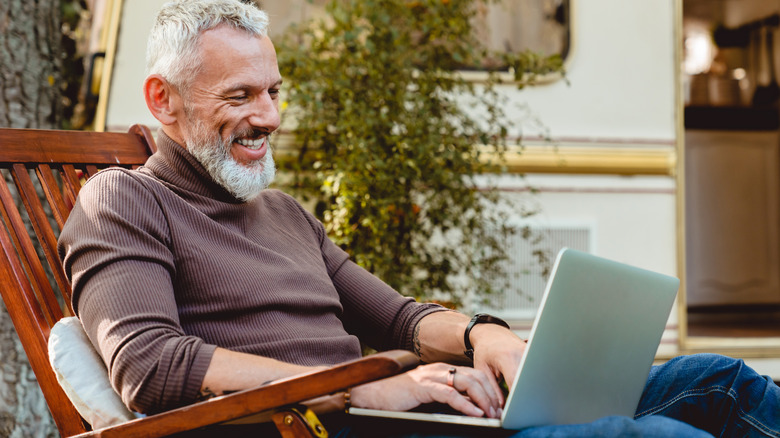 A smiling older man works on his laptop in front of an RV.