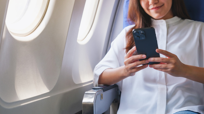 A woman using her cell phone while seated in her seat on a plane