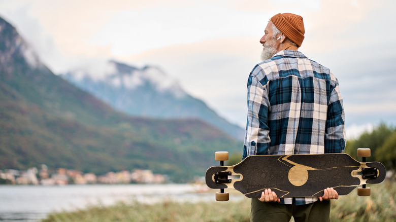 Old man holding skateboard in a mountain park