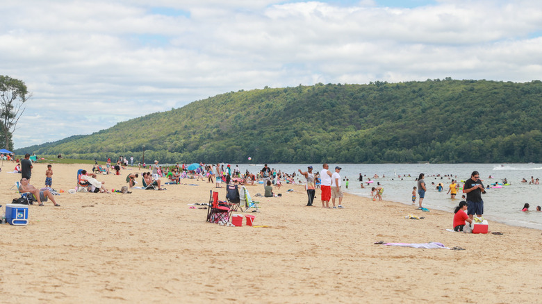 A busy beach with many people on the sand and in the water in Beltzville State Park.
