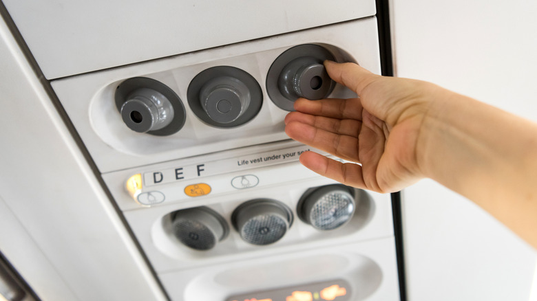 Hand turning the overhead air vent in an airplane