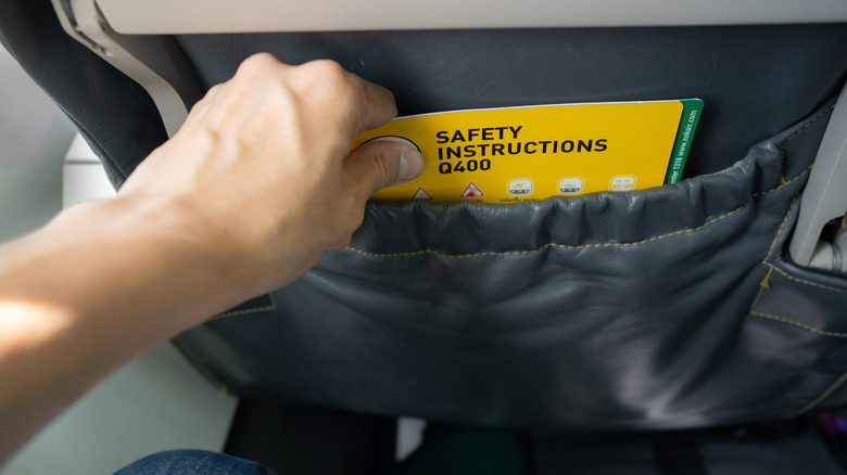 Person pulling out a safety instructions card from a seat back pocket