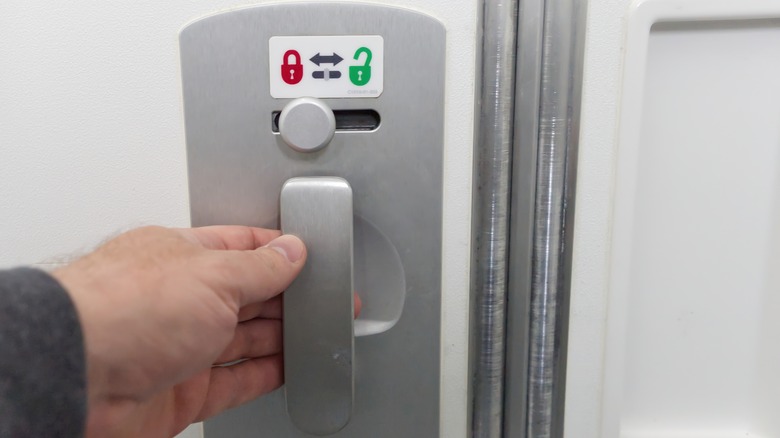 Hand touching the lavatory handle of an airplane bathroom