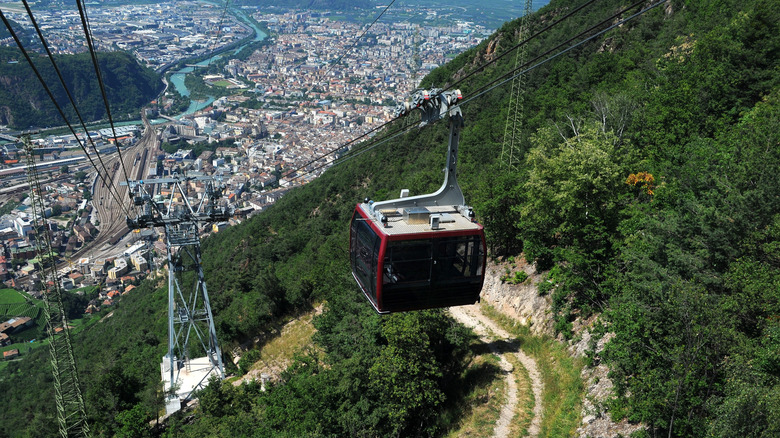 A red cable car against a view of Bolzano city below