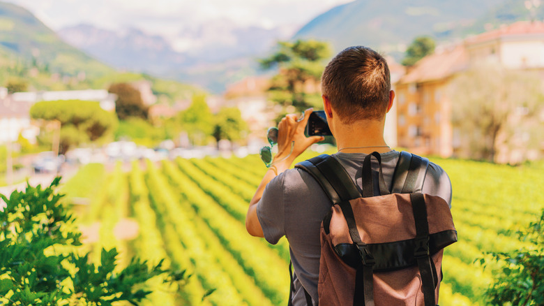 Backview of a tourist taking a photo of Bolzano's landscape in the summer.