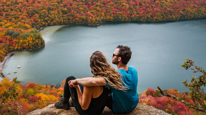 A young couple sitting on a mountaintop overlooking a Vermont lake and fall foliage