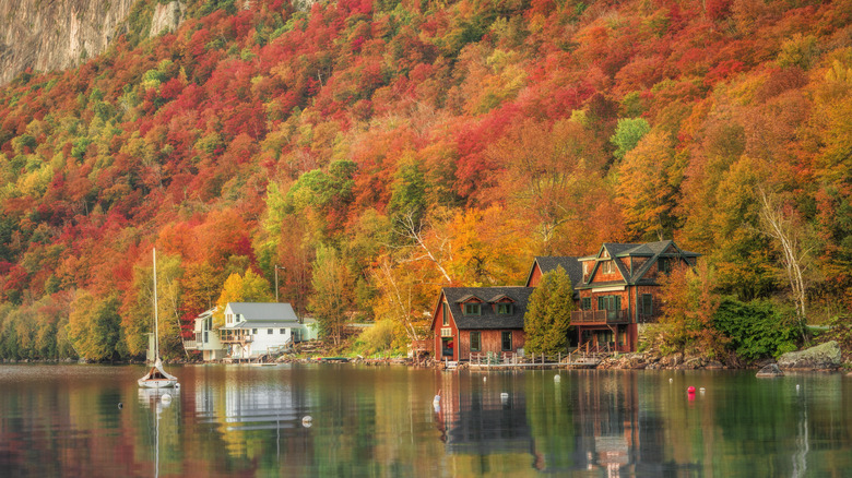 Lakeside houses and a sailboat on Lake Willoughby against a backdrop of Vermont's fall foliage