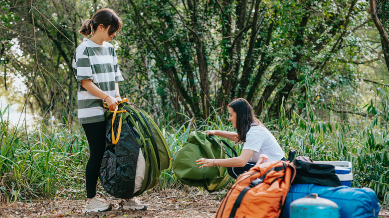 Two people camping in the woods with backpacks and equipment around them