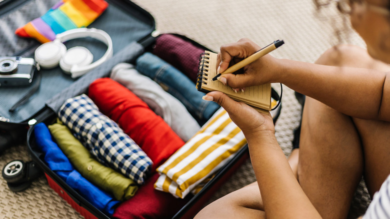Person with notebook and suitcase with rolled clothes.