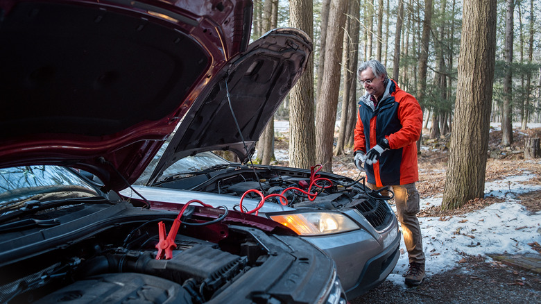 A man in an orange winter jacket jump starts a car in the snow.
