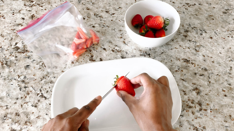 Prepping strawberries and storing them in a Ziploc bag.